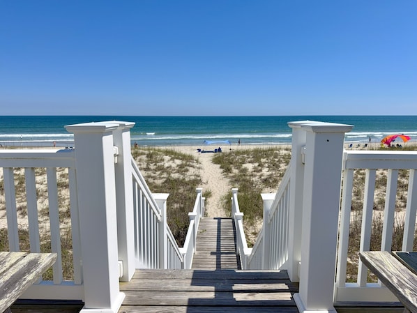 A wooden staircase leading to a beach with white railings.
