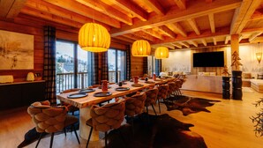 Un espace repas avec une longue table en bois, plusieurs chaises et des lampes suspendues.
