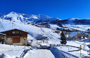 Une station de montagne enneigée, avec des bâtiments en bois, des remontées mécaniques et un ciel bleu dégagé.