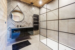 Une salle de bain moderne avec un pare-feu en mosaïque disposée en chevrons, un miroir rond, un porte-serviettes noir et un meuble-lavabo en verre.