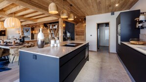 Une cuisine moderne dotée d’un grand îlot central, de poutres en bois au plafond, de luminaires suspendus et offrant une vue sur la salle à manger.