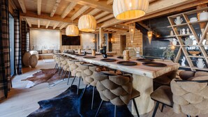 Un intérieur en bois avec une longue table à manger, de nombreuses chaises et des lampes suspendues.