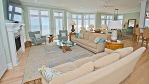 En rummelig stue med en stor beige sofa, to lænestole, et sofabord og en pejs.
