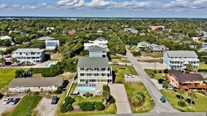 An aerial view of a coastal residential area with multiple houses and a large building with a pool.
