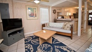 A living room with a television, a sofa, a coffee table, and a ceiling fan. - Beach Life Down, Oceanview Duplex in Atlantic Beach, NC! (Atlantic Beach)