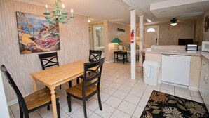 A dining area with a wooden table and chairs, a painting on the wall, a chandelier, and a kitchen area with a dishwasher. - Beach Life Down, Oceanview Duplex in Atlantic Beach, NC! (Atlantic Beach)