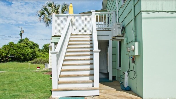 A wooden staircase leading to a green house with a white railing and a yellow umbrella on the roof. - Beach Life Down, Oceanview Duplex in Atlantic Beach, NC! (Atlantic Beach)