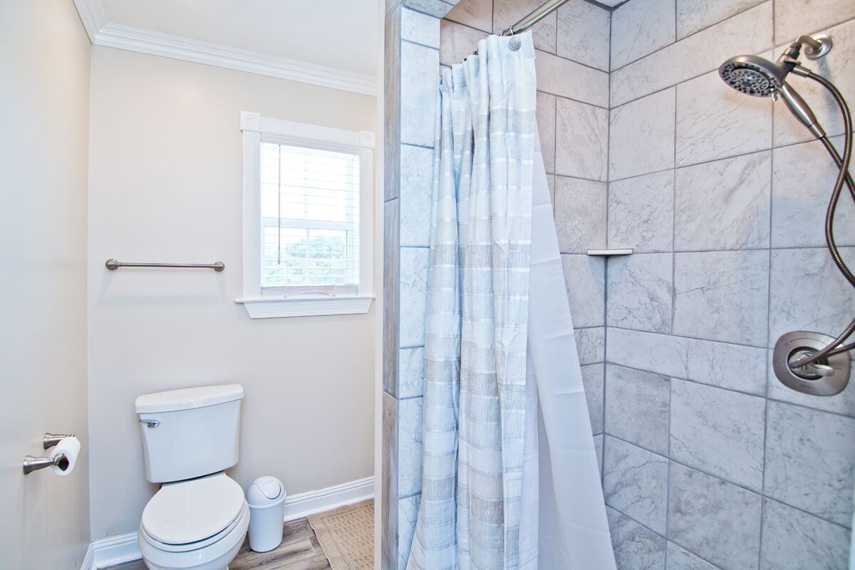 A bathroom with a toilet, a shower with a handheld showerhead, a window, and a towel rack.