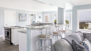 A modern kitchen with a central island, bar stools, and a view of the ocean. - Beach Thyme, Oceanfront House in Indian Beach, NC! (Indian Beach)
