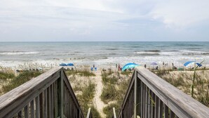A beach view with a wooden boardwalk leading to the shore, featuring umbrellas and beach chairs. - Beach Thyme, Oceanfront House in Indian Beach, NC! (Indian Beach)