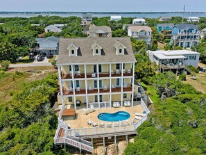 A multi-story house with a pool, surrounded by greenery and a view of the ocean. - Beached, Almost Oceanfront House in Emerald Isle, NC! (Emerald Isle)