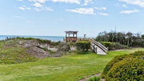 A beachside view with a wooden structure, a wooden bridge, and a well-maintained lawn. - Beachwalk 112, Oceanfront Condo in Pine Knoll Shores, NC! (Pine Knoll Shores)