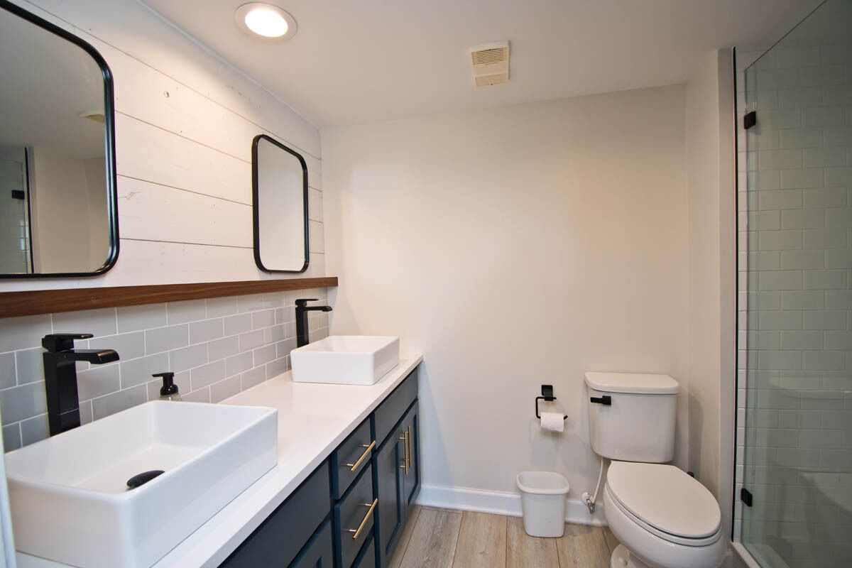 A modern bathroom with two sinks, a toilet, and a shower area.