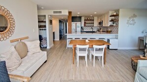 A modern kitchen with white cabinets, a wooden dining table, and a central island. - Beachwalk 116, Oceanfront Condo in Pine Knoll Shores, NC! (Pine Knoll Shores)