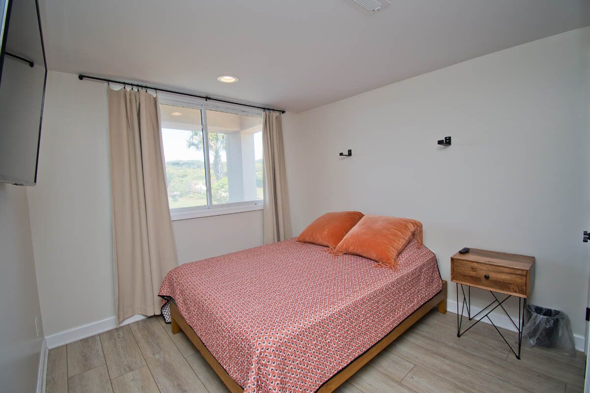 A bedroom with a bed, a nightstand, a window with curtains, and a ceiling light.