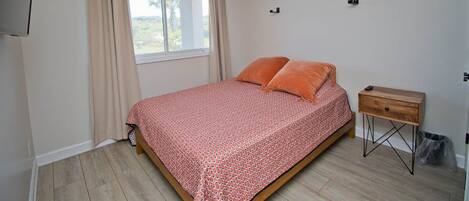 A bedroom with a bed, a nightstand, a window with curtains, and a ceiling light.