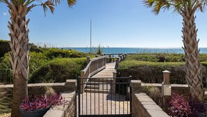 A wooden boardwalk leading to a beach with palm trees and a clear sky.