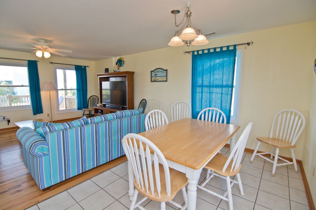 Un comedor con una mesa de madera y sillas blancas, un sofá a rayas y un televisor sobre un mueble de madera.