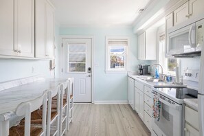 A kitchen with white cabinets, a marble countertop, and a dining area with white chairs. - Better Daze, Oceanfront House in Emerald Isle, NC! (Emerald Isle)