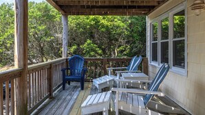 A wooden deck with Adirondack chairs and a table, overlooking a wooded area.