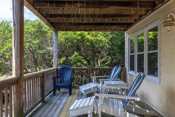 A wooden deck with Adirondack chairs and a table, overlooking a wooded area. - Big Kahuna, Oceanview House in Emerald Isle, NC! (Emerald Isle)
