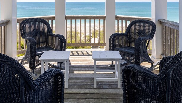 A covered outdoor seating area with wicker chairs and a small table, overlooking the ocean. - Bliss By The Beach, Oceanfront House in Emerald Isle, NC! (Emerald Isle)