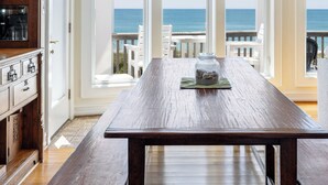 A spacious dining area with a view of the ocean, wooden cabinets, and a large table. - Bliss By The Beach, Oceanfront House in Emerald Isle, NC! (Emerald Isle)