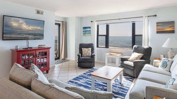 A living room with a view of the sea, a red cabinet, and a grey armchair.