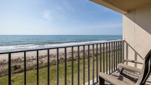 A balcony with a view of the ocean, a wooden bench, and a railing.