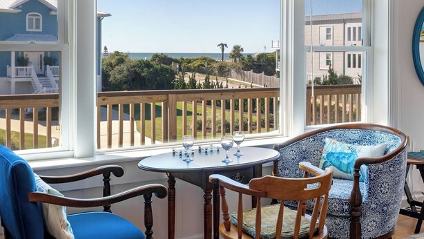 Una sala de estar con ventanales con vistas a una zona residencial, una terraza de madera y una mesa con vasos.