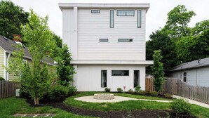 A modern two-story house with a flat roof, a front porch, and a small circular garden area.
