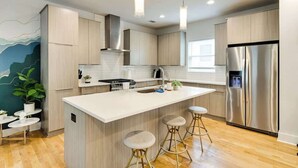 A modern kitchen with a central island, stainless steel appliances, and light wood cabinetry.