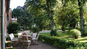 Un patio exterior con suelo de ladrillo, rodeado de abundante vegetación y árboles.