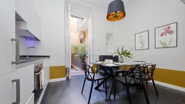 Cozinha moderna com área de jantar, com esquema de cores preto e branco, mesa de jantar com cadeiras e luminária pendente.