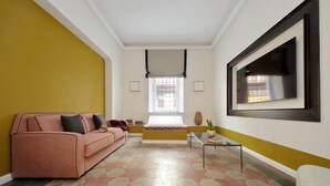 Uma sala de estar com um sofá, uma mesa de centro e uma televisão fixada na parede.