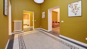 Um corredor com tapete estampado, radiador e quadros nas paredes.