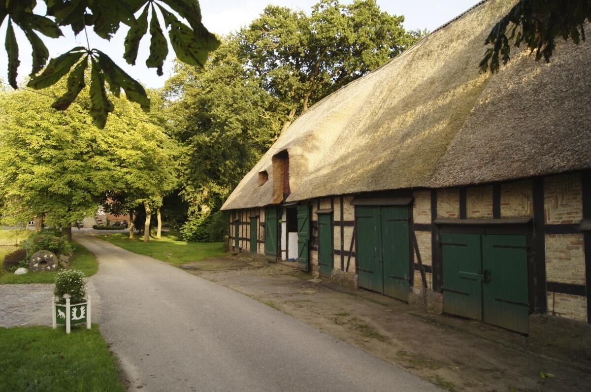 Un bâtiment traditionnel à toit de chaume, accessible par un chemin étroit, et entouré de verdure.