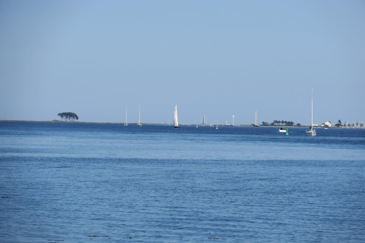 A coastal view with a calm sea, a lighthouse, and several sailboats.