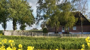 A rural house with a brick exterior, surrounded by a wooden fence and lush greenery.