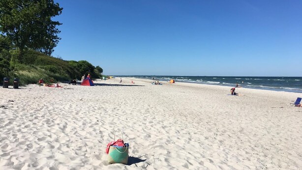 Uma praia com uma tenda, uma bolsa e pessoas relaxando.