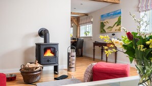 A cozy living room with a wood-burning stove, a dining area with a table and chairs, and a vase with flowers on a table.