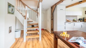 A modern kitchen with white cabinets, a wooden table, and a staircase with wooden railings.