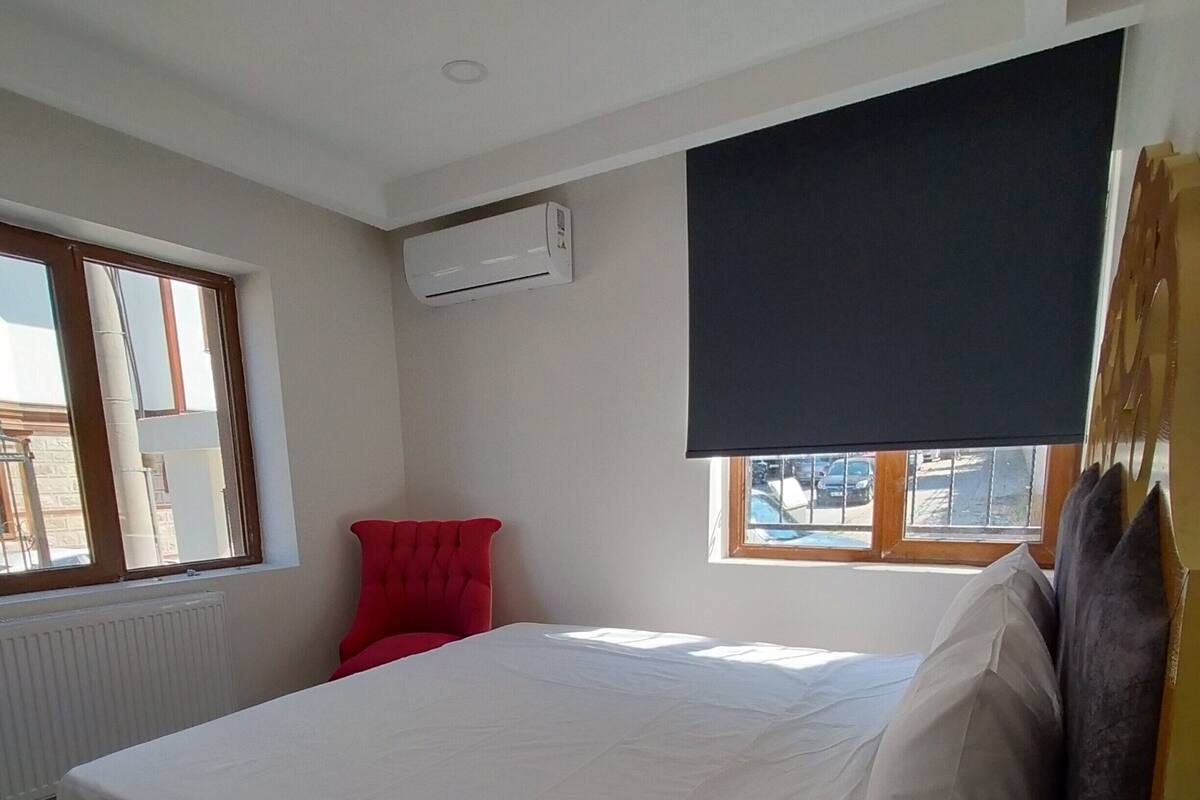 A bedroom with a large bed, a red chair, a window, and an air conditioning unit.