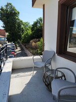A balcony with wicker chairs and a table, a parked car, and a building in the background.