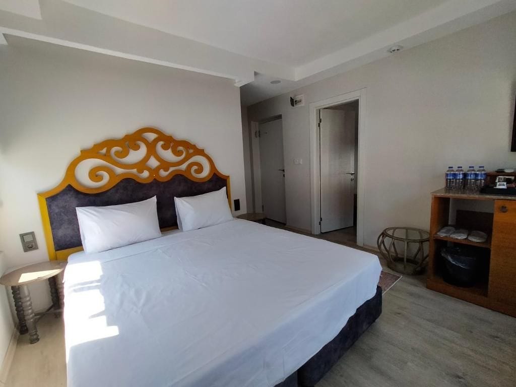 Une chambre d’hôtel avec un grand lit, une tête de lit en bois, une table de chevet, une armoire et une porte donnant sur une autre pièce.
