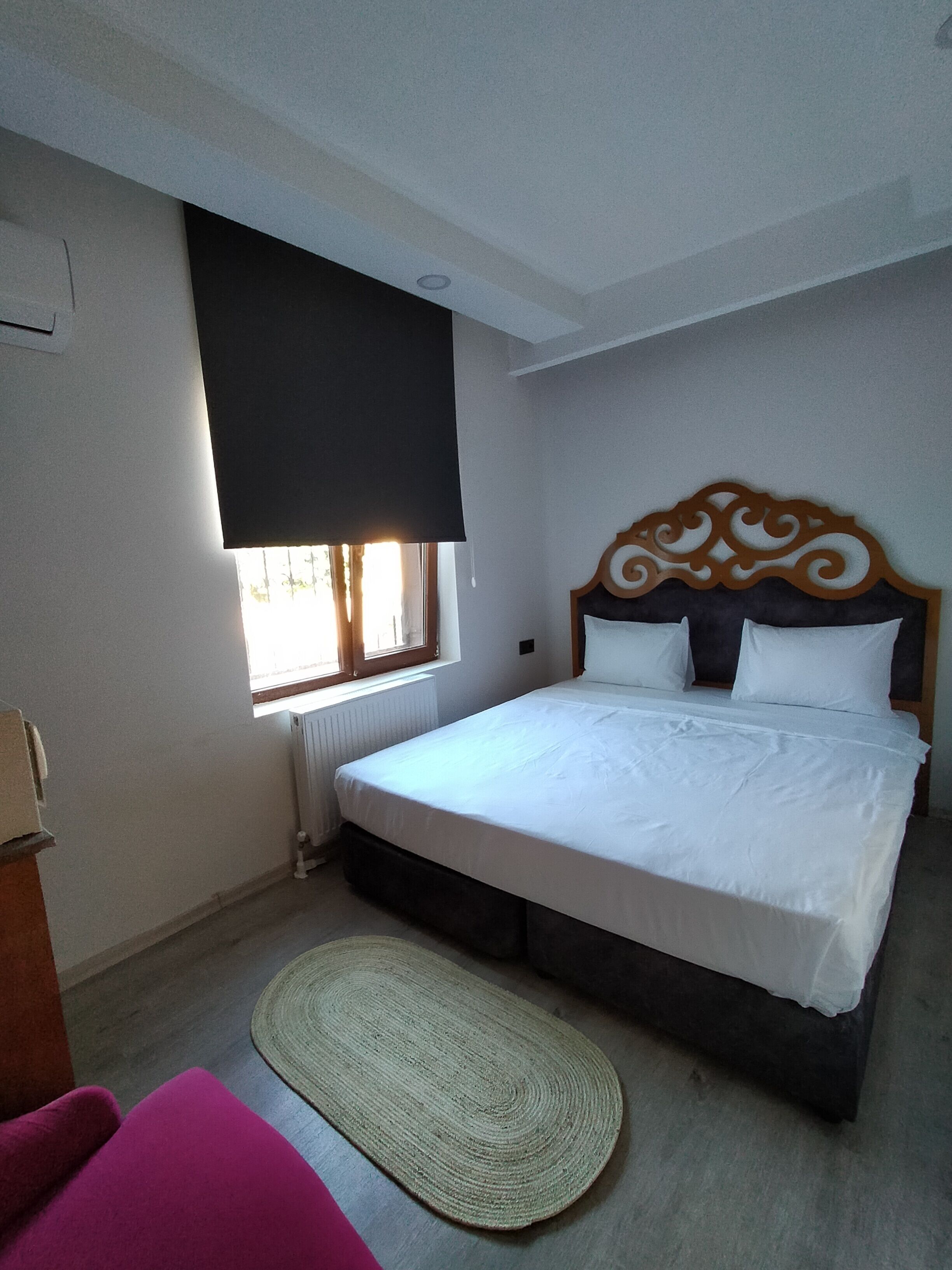 Un dormitorio con cama, ventana con persiana, radiador y alfombra.