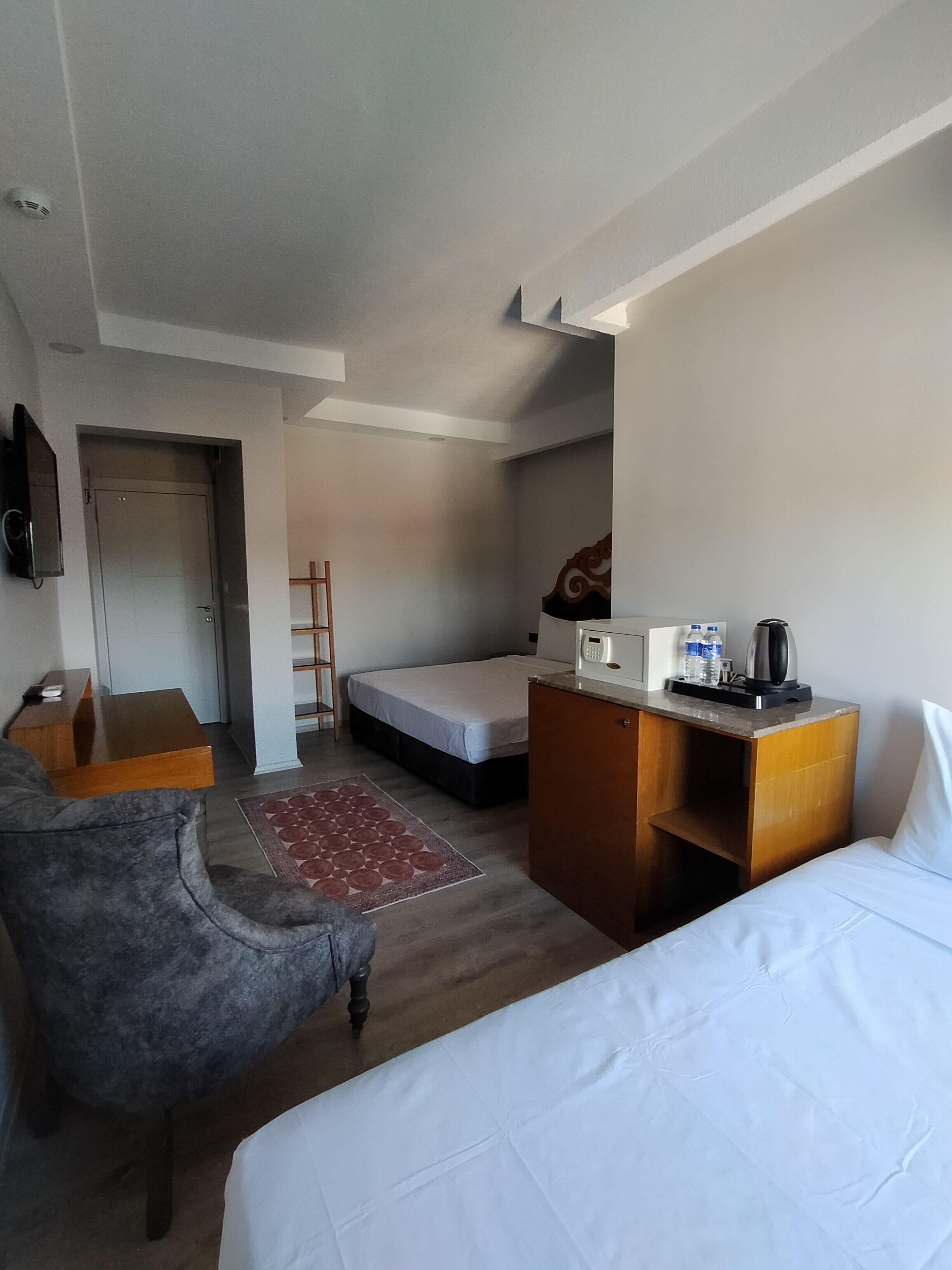 A hotel room with a bed, a desk, a chair, a small kitchenette, and a TV.