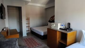 A hotel room with a bed, a desk, a chair, a small kitchenette, and a TV.
