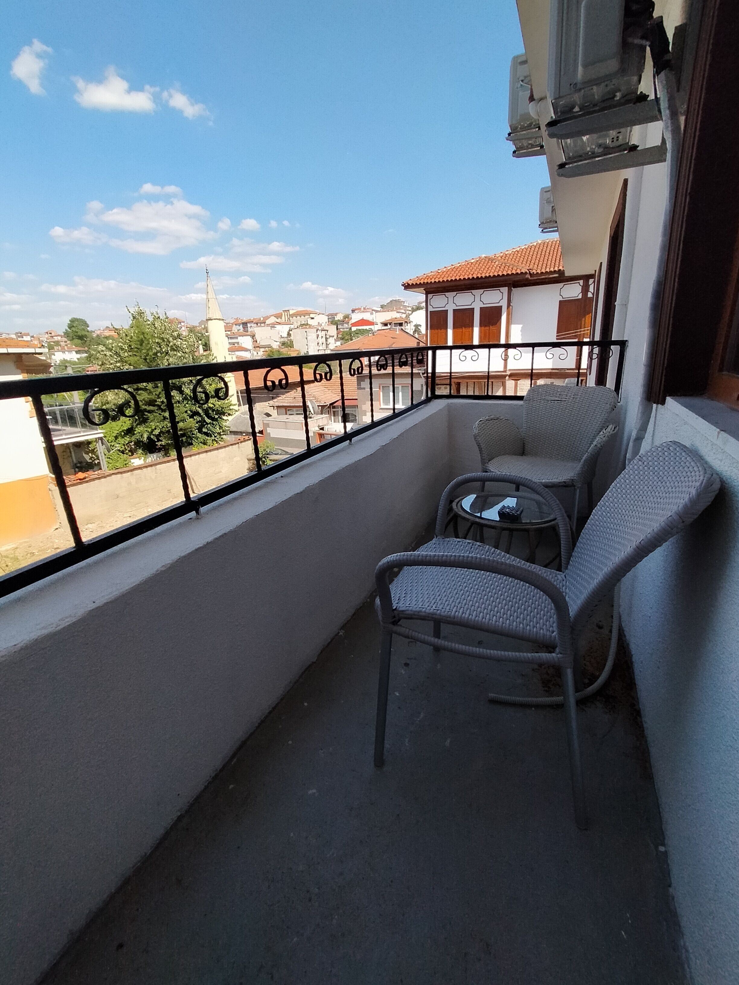 Un balcon agrémenté de meubles en osier, d’une petite table et offrant une vue sur le paysage urbain.