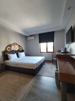 A hotel room with a bed, a desk, a chair, a TV, and a window with blinds.